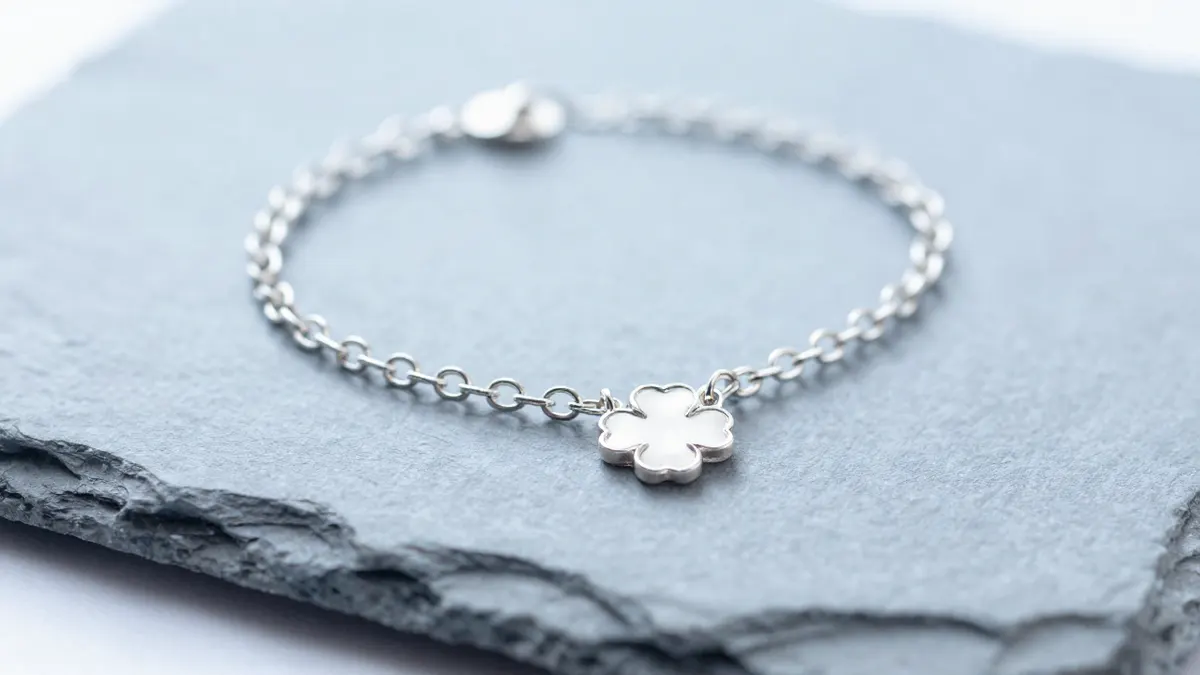 Sterling silver lucky clover anklet with tiny charms draped over warm sand in golden summer light