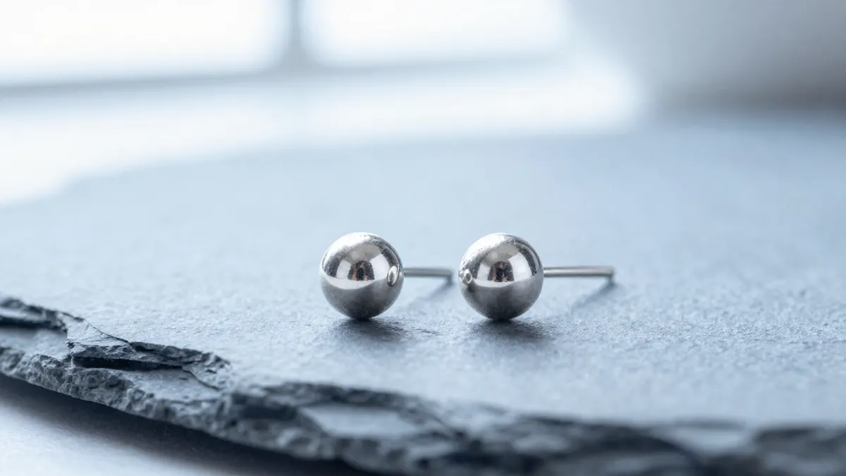 Pair of small polished 925 silver ball ear pins resting on a white dish in soft daylight