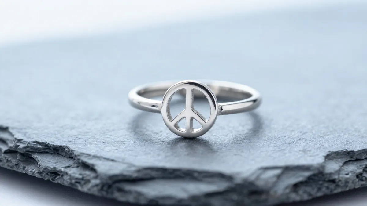 Silver peace sign ring worn on a toe with bare foot resting on white sand at the beach