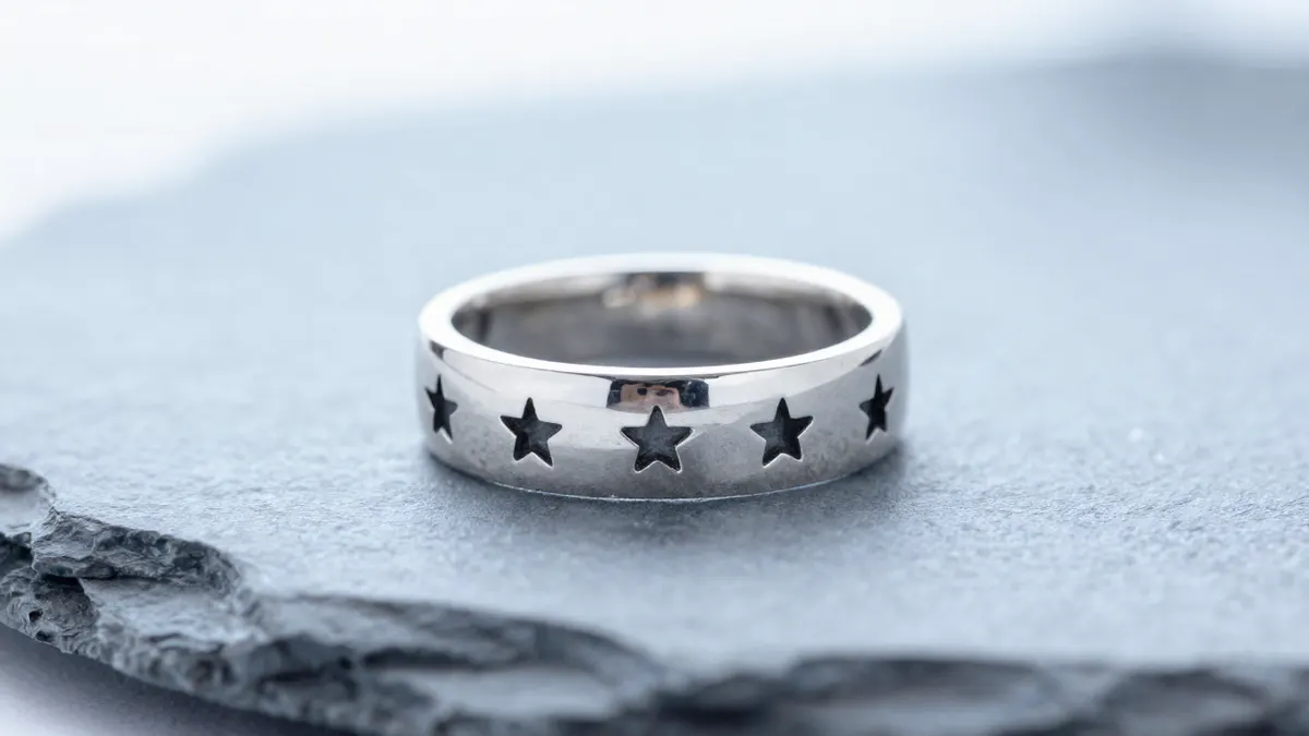 Band of stars ring in sterling silver with a row of small star motifs on dark slate under cool light