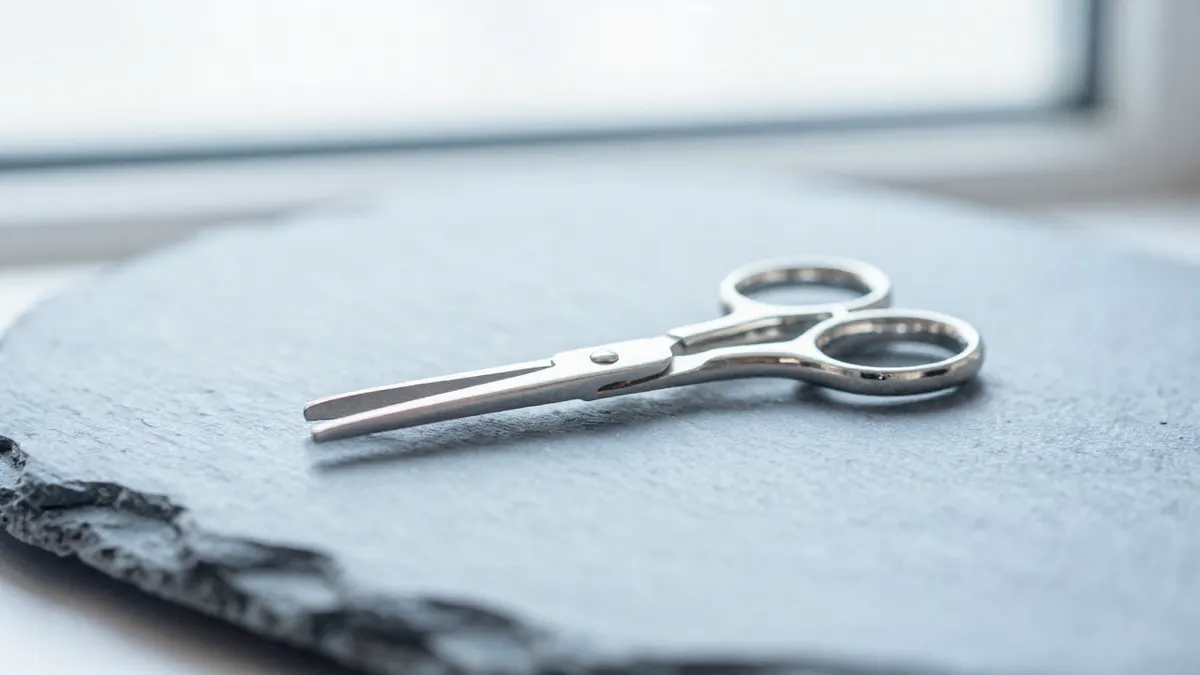 Sterling silver scissors ring with open slender blades resting on a wooden workbench beside a thread spool