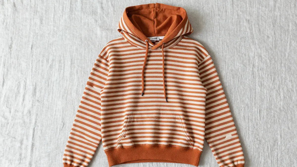 Cream pumpkin spice hoodie with striped knit panel and lace-up front cords hanging near a window