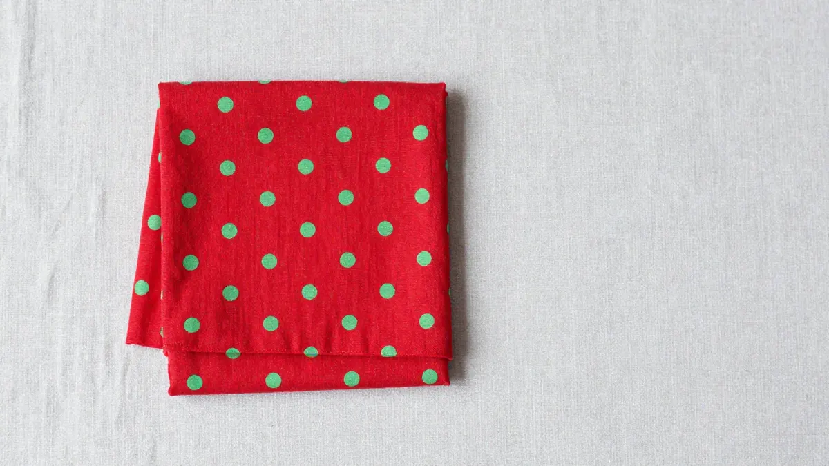 Red dress with white polka dots and a retro silhouette hanging on a wooden rack in a sunlit boutique